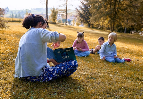 marta di slegato legge un libro a gruppo di bambini sul prato