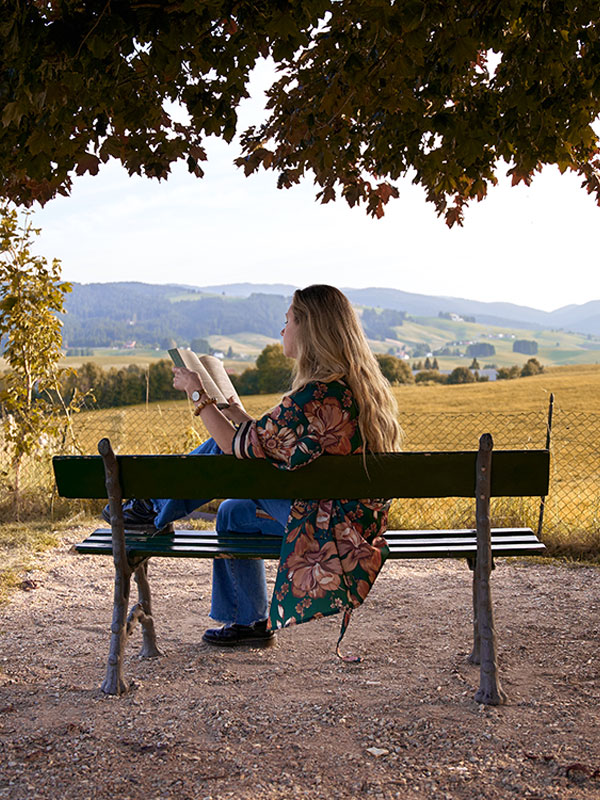 ragazza che legge libro di narrativa su panchina al parco