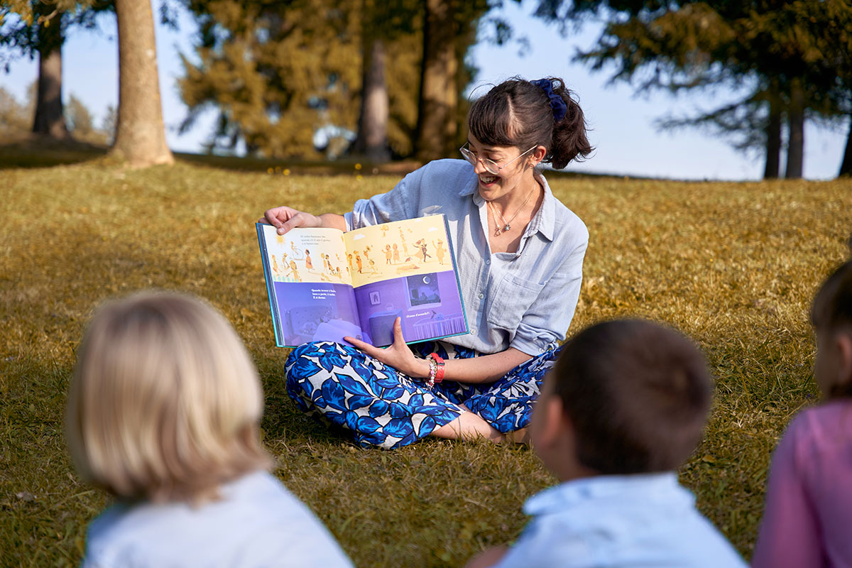 marta paganin di slegato mostra albo illustrato a bambini seduti al parco