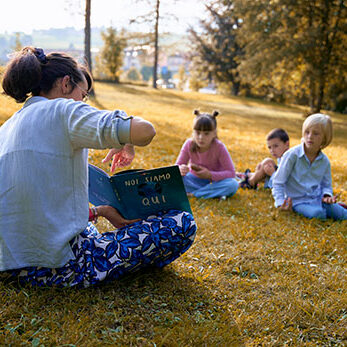 marta di slegato legge un libro a gruppo di bambini sul prato